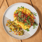 Seared salmon with corn relish, red pepper strips and microgreens on a white plate
