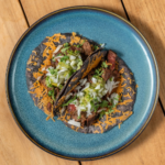 Asada vampiro tacos topped with melted cheese and cilantro on a blue plate