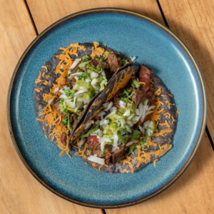 Asada vampiro tacos topped with melted cheese and cilantro on a blue plate