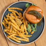 Bacon-jam burger on a brioche bun with a side of seasoned fries on a blue plate