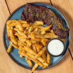 Sliced steak with truffle fries and a side of dipping sauce on a blue plate