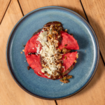 Pork belly served over a bright red sauce and finished with shredded cheese on a blue plate