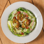 Little Gem lettuce salad with grilled chicken, tomato and creamy dressing on a white plate