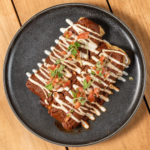 Shrimp enchiladas drizzled with cream sauce and topped with microgreens on a dark plate