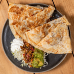 Lobster quesadilla wedges served with guacamole and pico de gallo on a dark plate