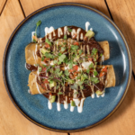 Mole short rib enchiladas with a cream drizzle and microgreens on a blue plate