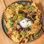 Onda Nachos piled with melted cheese, black beans, pico de gallo and sour cream on a blue platter