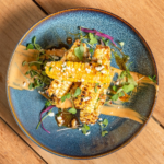 Elote corn riblets topped with herbs and microgreens on a blue plate