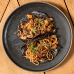 Spicy shrimp tacos piled with crispy onion strands on a black plate