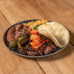 Steak and lobster plate with grilled peppers and a warm flour tortilla on a dark oval plate
