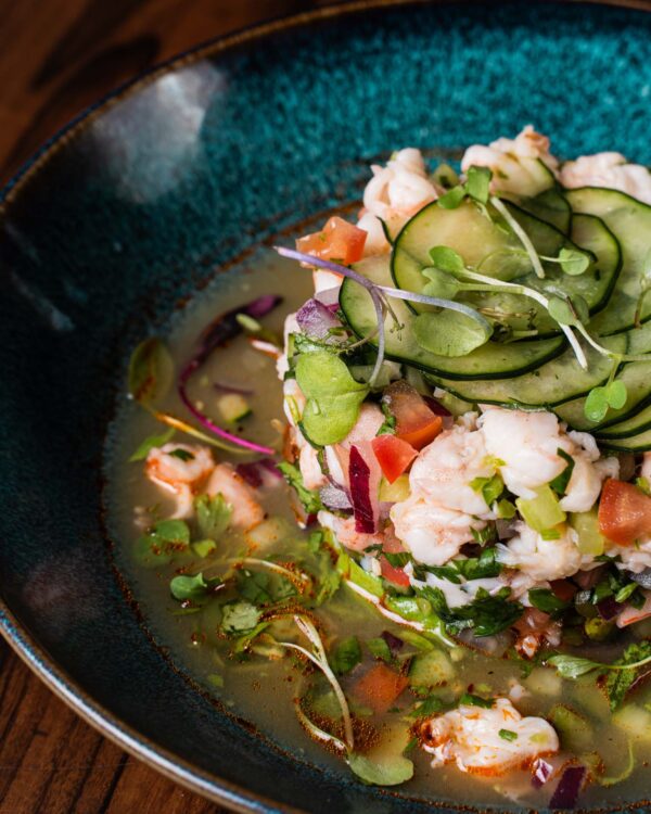 Close-up of ceviche with shrimp, tomato, red onion and fanned cucumber in a teal bowl