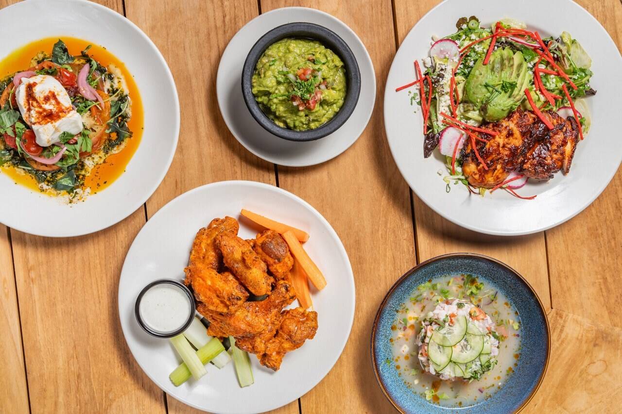 Overhead spread of Casa de Onda dishes on a patio table, wings, guacamole, ceviche and salads