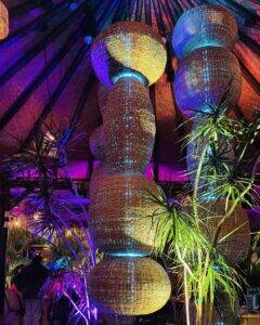 The rattan pendant chandelier lit teal and purple under the palapa at Casa de Onda