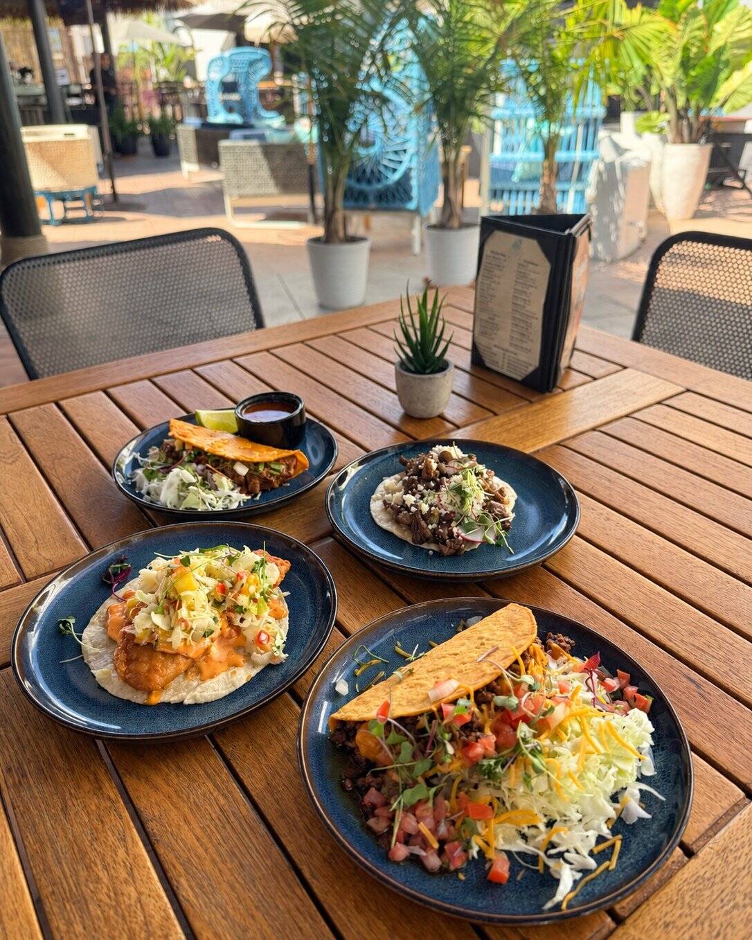 The four Tulum Tuesday tacos on blue plates on a teak patio table at Casa de Onda
